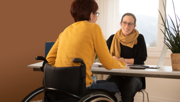 Eine Beratungsfachperson im Gespräch mit einer Frau im Rollstuhl